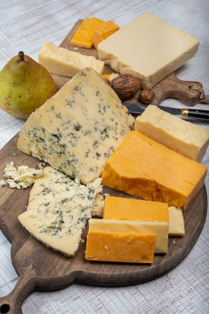 English cheeses collection, mature and colored cheddar cheese and semi-soft, crumbly old stilton blue cheese close up on plateの写真素材
