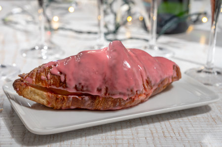 New year party, sweet dessert pink creamy croissant and brut champagne cava or prosecco wine in tulip glasses with garland lights on backgroundの写真素材