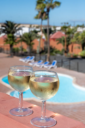 Glasses of cold white wine on roof terrace served outdoor, view on Corralejo, Fuerteventura in sunny day, pool with blue waterの写真素材