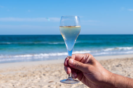 Hand with glass of cava, champagne sparkling wine on vacation, Dunes Corralejo sandy beach, Fuerteventura, Canary islandsの写真素材