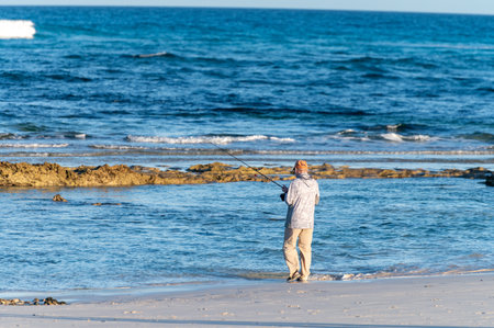 Retired old man fishing in winter in Corralejo dunes on white sandy beach, blue water, Fuerteventura, Canary islands, Spain in winterの写真素材