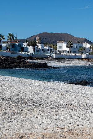 Walking on sea promenade in Corralejo town along white popcorn beach with white corals, black rocks, blue water, Fuerteventura, Canary islands, Spainの写真素材