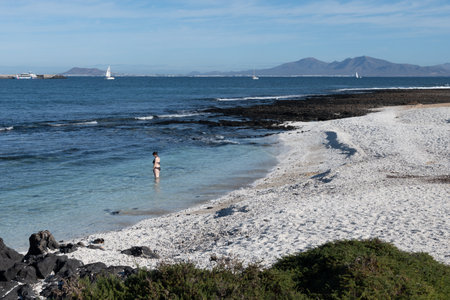 Walking on sea promenade in Corralejo town along white popcorn beach with white corals, black rocks, blue water, Fuerteventura, Canary islands, Spainの写真素材