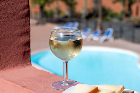Glasses of cold white wine on roof terrace served outdoor, view on Corralejo, Fuerteventura in sunny day, pool with blue waterの写真素材
