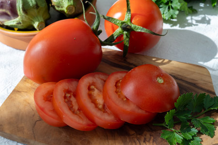 Ripe red Roma tomatoes in bowl with fresh herbs on tableの写真素材