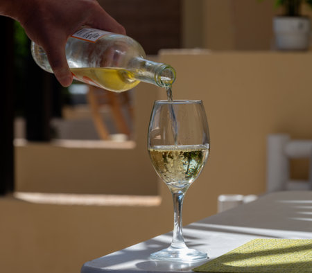 Waiter pouring white wine into glass on white terrace table outdoor in sunny dayの写真素材
