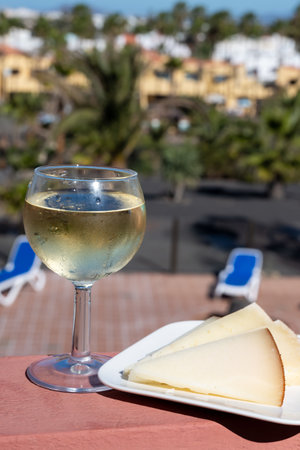 Spanish hard manchego, cow, sheep and goat cheese, glass of cold white wine and blue swimming pool on backgroundの写真素材