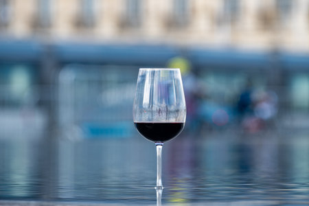 Tasting of Bordeaux blended red wine with wine city Bordeaux on background, left bank of Gironde Estuary, France. Glass of red French wine served outdoor.の写真素材