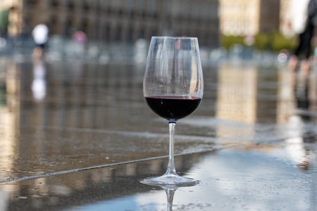 Tasting of Bordeaux blended red wine with wine city Bordeaux on background, left bank of Gironde Estuary, France. Glass of red French wine served outdoor.の写真素材