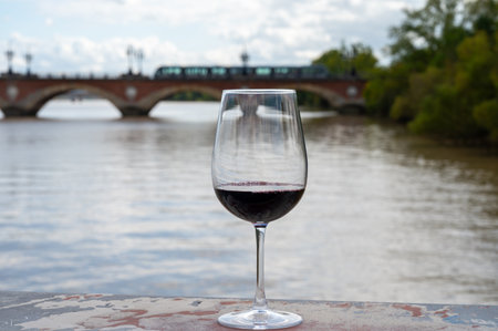 Tasting of Bordeaux blended red wine with wine city Bordeaux on background, left bank of Gironde Estuary, France. Glass of red French wine served outdoor.の写真素材