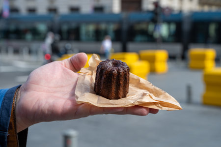 Canele, French pastry flavored with rum and vanilla, soft and tender custard center and dark, caramelized crust specialty of Bordeaux region, France and streets of Bordeaux on backgroundの写真素材