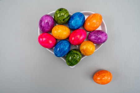 Colorful Easter eggs on table for celebration of catholic Easter in April, heart shape plate, copy...