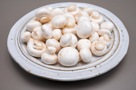 White champignon mushrooms fresh uncooked on white ceramic plate copy space on gray backgroundの写真素材