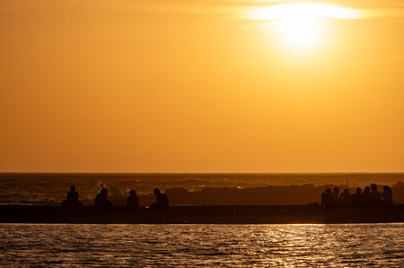 Man and woman staying and looking at sunset on ocean beach, orange sky, silhouettes of people on vacation, Canary islandsの写真素材