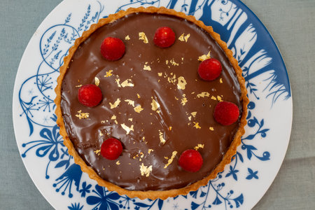 Chocolate cake with apricot jam decorated with fresh raspberry and 24-karat gold plaques on blue white boardの写真素材