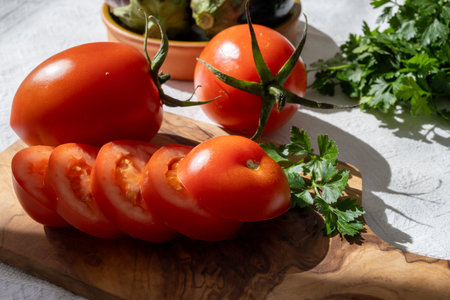 Ripe red Roma tomatoes in bowl with fresh herbs on tableの写真素材