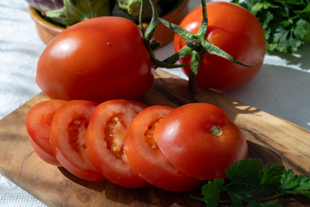 Ripe red Roma tomatoes in bowl with fresh herbs on tableの写真素材
