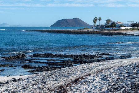 Walking on sea promenade in Corralejo town along white popcorn beach with white corals, black rocks, blue water, Fuerteventura, Canary islands, Spainの写真素材