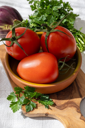 Ripe red Roma tomatoes in bowl with fresh herbs on tableの写真素材