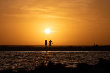 Man and woman staying and looking at sunset on ocean beach, orange sky, silhouettes of people on vacation, Canary islandsの写真素材