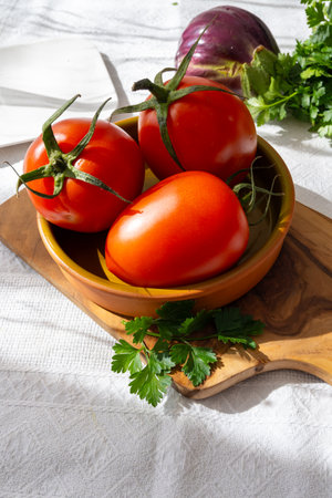 Ripe red Roma tomatoes in bowl with fresh herbs on tableの写真素材