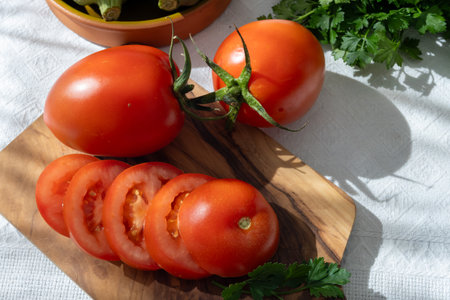 Ripe red Roma tomatoes in bowl with fresh herbs on tableの写真素材