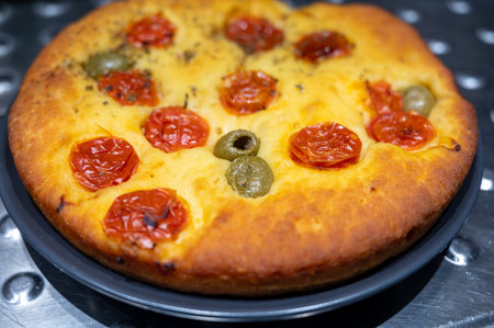 Tasty italian vegetarian food, fresh baked flat foccachia bread with small cherry tomatoes, olives and herbs close upの写真素材
