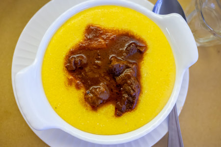 Traditional first course for lunch or dinner in Italy, yellow corn polenta porridge with stew served in Italian restaurant, Milan, Italy, close upの写真素材