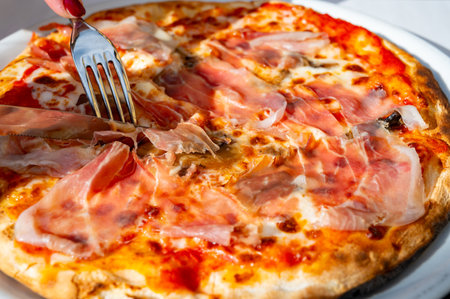 Eating of fresh baked pizza dish in italian pizzeria restaurant with cheese and Prosciutto di Parmaの写真素材