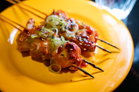 Wooden skewers with pieces of chicken fillet in teriyaki sauce from the grill served at yakitori restaurant in Milan, Italy, close upの写真素材