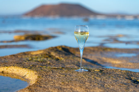 Glass of cava or champagne sparkling wine, winter vacation, low tide on Dunes Corralejo sandy beach, Fuerteventura, Canary islands, Spainの写真素材