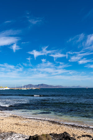 Walking on sea promenade in Corralejo along black rocks, blue water, view on volcanic Lanzarote island, Fuerteventura, Canary islands, Spainの写真素材