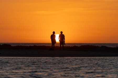 Man and woman staying and looking at sunset on ocean beach, orange sky, silhouettes of people on vacation, Canary islandsの写真素材