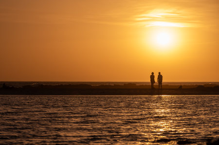 Man and woman staying and looking at sunset on ocean beach, orange sky, silhouettes of people on vacation, Canary islandsの写真素材