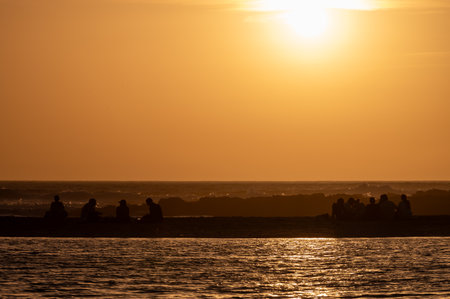 Man and woman staying and looking at sunset on ocean beach, orange sky, silhouettes of people on vacation, Canary islandsの写真素材