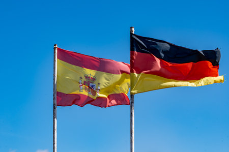 Spanish and German flags on flagstaff and blue sky copy spaceの写真素材