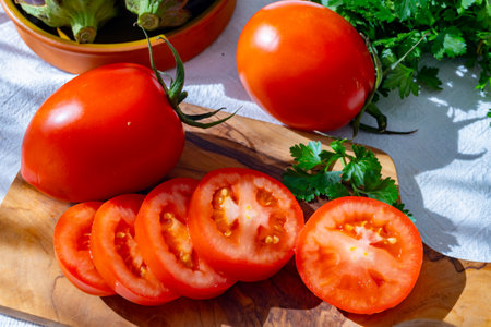 Ripe red Roma tomatoes in bowl with fresh herbs on tableの写真素材