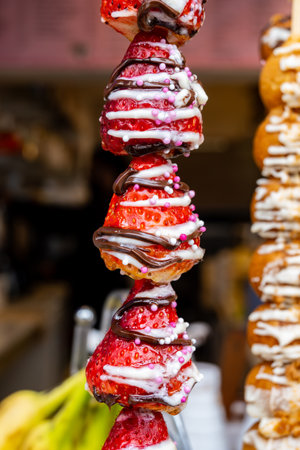 Candy shop in London, various sweet profiteroles and fresh strawberries with chocolate decoration on skewers ready to eatの写真素材
