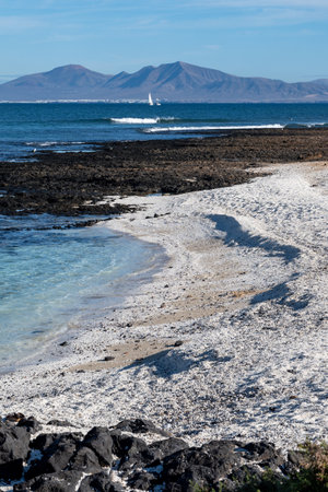 Walking on sea promenade in Corralejo town along white popcorn beach with white corals, black rocks, blue water, Fuerteventura, Canary islands, Spainの写真素材