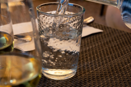 Waiter pouring mineral water from the glass bottle into a glass, food concept, close upの写真素材