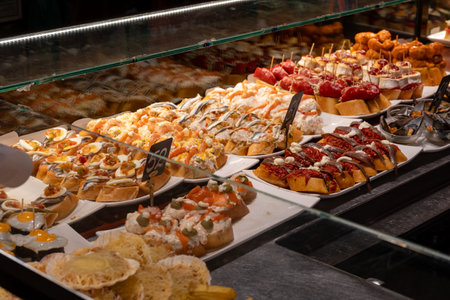Typical snacks of Basque Country, variety of pinchos or pinxtos oven baked seafood, bread, skewers with jamon, goat cheese served in bar in San-Sebastian or Bilbao, Spain, close upの写真素材