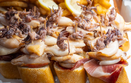 Typical snacks of Basque Country, pinchos or pinxtos skewers with small pieces of bread, fish, sea food, sweet green pepper served in bar in San-Sebastian or Bilbao, Spain, close upの写真素材