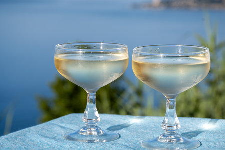 Cold sparkling wine, cava or champagne in two coupe glasses on table with blue sea viewの写真素材