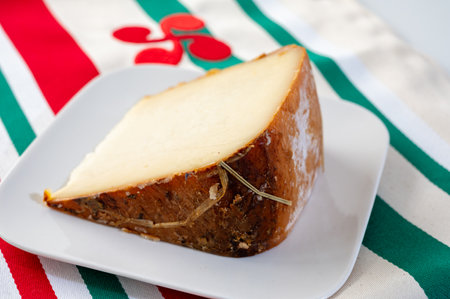 Piece of tasty Basque Brebis Fume smoked sheep cheese produced in south-western France, Northern Basque Country and towel with Basque symbol and colors close upの写真素材