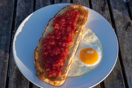 Traditional andalusian breakfast on roof patio with bread toasts, fresh ground tomatoes sauce and olive oil, roasted egg, Sevilla, Andalusia, south of Spainの写真素材