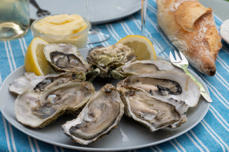 Plate with fresh live raw oysters seashells with citron, bread, butter and white wine served at...