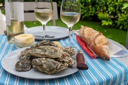 Plate with fresh live raw oysters seashells with citron, bread, butter and white wine served at...
