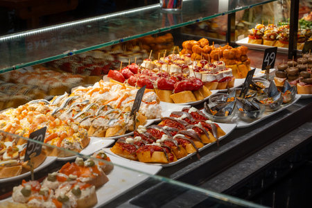 Typical snacks of Basque Country, variety of pinchos or pinxtos oven baked seafood, bread, skewers with jamon, goat cheese served in bar in San-Sebastian or Bilbao, Spain, close upの写真素材