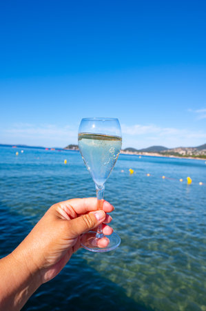Summer time in Provence, hand with glass of cold champagne cremant sparkling wine on famous Pampelonne white sandy beach near Saint-Tropez in sunny day, Var department, France, beach club partyの写真素材