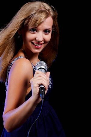a charming young blonde on a black background with a microphoneの写真素材